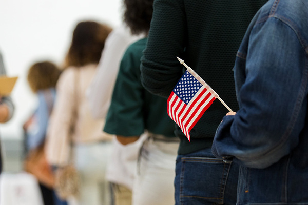 A view of a line of people from a back angle. Most are out of focus. The person in back holds a small American flag.